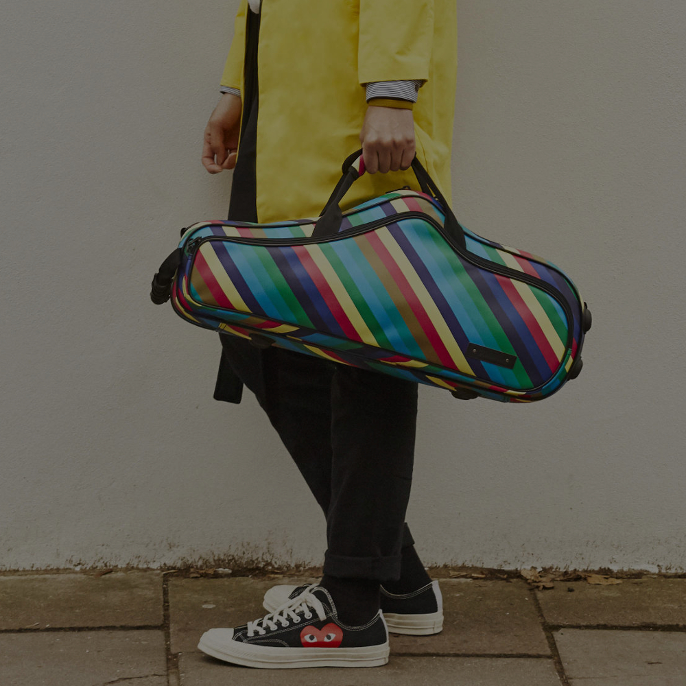 Man leaning against a wall with candy band saxophone case